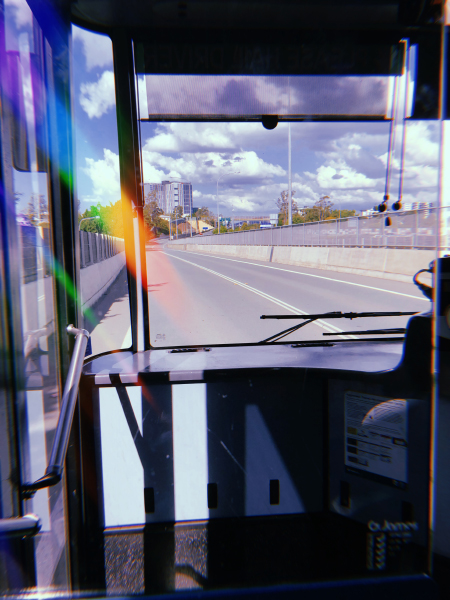 a photo taken out the front window of a bus. you can see the road ahead and some buildings in the distance